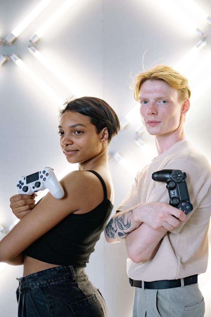 Two young adults holding game controllers, posing confidently in a modern studio setting.