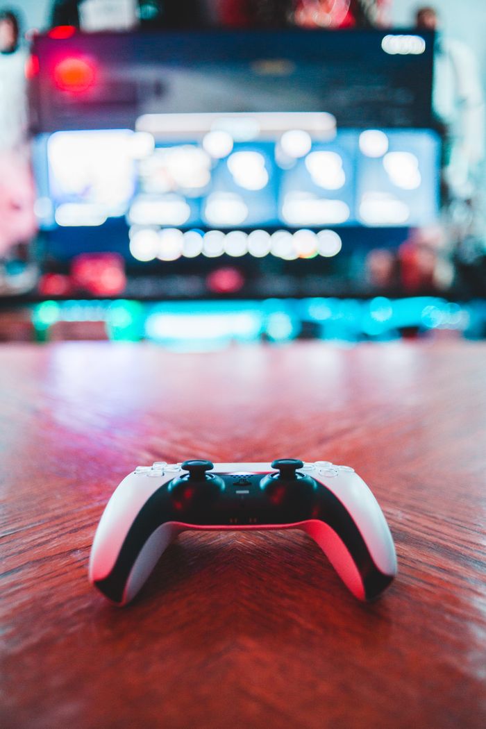 services-03 A close-up of a gaming controller on a wooden table with vibrant screen in the background.